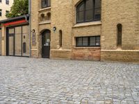 a brick paved street near an old building with windows and a door at the corner