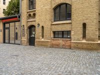 a brick paved street near an old building with windows and a door at the corner