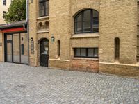 a brick paved street near an old building with windows and a door at the corner