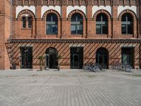 the brick building is near several bicycles parked outside of it the buildings have multiple arched windows