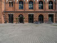 the brick building is near several bicycles parked outside of it the buildings have multiple arched windows