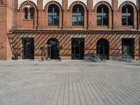 the brick building is near several bicycles parked outside of it the buildings have multiple arched windows