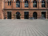 the brick building is near several bicycles parked outside of it the buildings have multiple arched windows