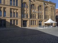 the large brick building has an awning outside of it next to a sidewalk with a bench and chairs