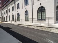 a person is riding a skateboard on the sidewalk near an old brick building while another passes by