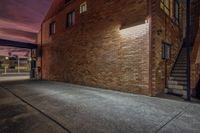 a dark alley leading to a brick building and some stairs, which leads up to a balcony