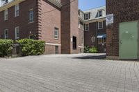 brick building next to green and white door and plant in front of sidewalk with brick path between buildings