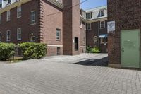 brick building next to green and white door and plant in front of sidewalk with brick path between buildings