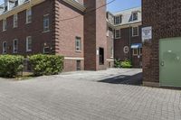 brick building next to green and white door and plant in front of sidewalk with brick path between buildings