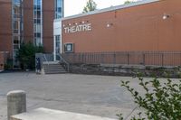 a sidewalk area outside a brick building that's written in theatre, with stairs going up to the right and two signs on the side