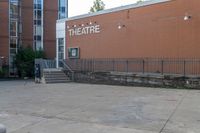 a sidewalk area outside a brick building that's written in theatre, with stairs going up to the right and two signs on the side