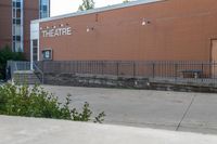 a sidewalk area outside a brick building that's written in theatre, with stairs going up to the right and two signs on the side