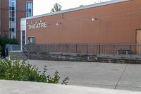 a sidewalk area outside a brick building that's written in theatre, with stairs going up to the right and two signs on the side