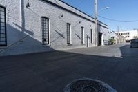 a sidewalk with some shadows on it near a brick building and electrical wires in the sky