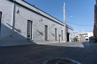 a sidewalk with some shadows on it near a brick building and electrical wires in the sky