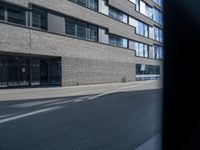 the street has a brick building and lots of windows in it, and a bus is moving by