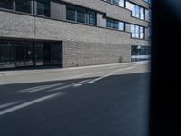 the street has a brick building and lots of windows in it, and a bus is moving by