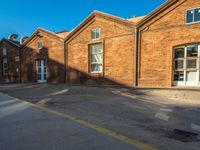 an empty street with tall brick buildings in the background while sunlight filters through windows and shadows across the walkway