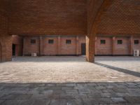 an empty brick courtyard with two wooden pillars in the middle of it and windows on either side