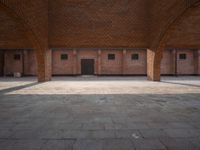 an empty brick courtyard with two wooden pillars in the middle of it and windows on either side