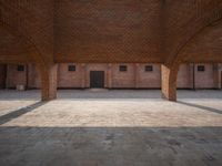 an empty brick courtyard with two wooden pillars in the middle of it and windows on either side