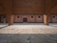 an empty brick courtyard with two wooden pillars in the middle of it and windows on either side