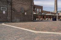 brick courtyard with red stone flooring in front of a factory building and silos