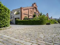 a large brick driveway that goes across the side of a building and a hedge lined parking lot