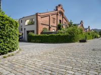 a large brick driveway that goes across the side of a building and a hedge lined parking lot