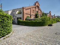 a large brick driveway that goes across the side of a building and a hedge lined parking lot