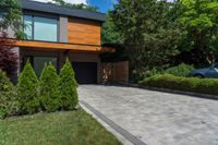 a driveway with brick pathway near two bushes and cars parked outside the house in the evening