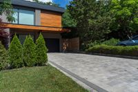 a driveway with brick pathway near two bushes and cars parked outside the house in the evening