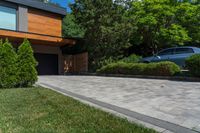 a driveway with brick pathway near two bushes and cars parked outside the house in the evening