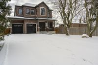 an empty lot with a brick house and garage covered in snow and footprints of a deer