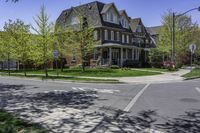 a two story brick house on an upscale street corner with grass and trees surrounding the house