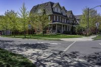 a two story brick house on an upscale street corner with grass and trees surrounding the house