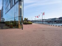 a brick pathway is seen along the water edge with flags and flags hanging on the buildings