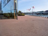 a brick pathway is seen along the water edge with flags and flags hanging on the buildings