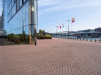 a brick pathway is seen along the water edge with flags and flags hanging on the buildings