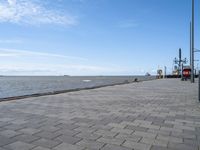 the sidewalk has brick pavers on it near a water front and the lighthouse in the distance