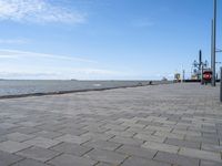 the sidewalk has brick pavers on it near a water front and the lighthouse in the distance