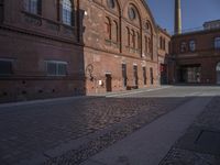 there is a brick road in the middle of town near the tall building that houses the factory and warehouse