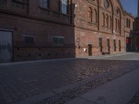 there is a brick road in the middle of town near the tall building that houses the factory and warehouse