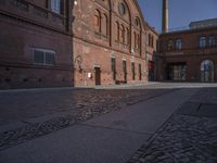 there is a brick road in the middle of town near the tall building that houses the factory and warehouse