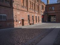 there is a brick road in the middle of town near the tall building that houses the factory and warehouse