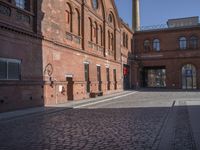 there is a brick road in the middle of town near the tall building that houses the factory and warehouse