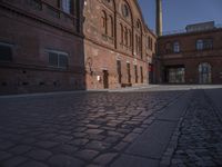 there is a brick road in the middle of town near the tall building that houses the factory and warehouse