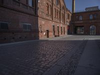 there is a brick road in the middle of town near the tall building that houses the factory and warehouse