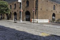 an intersection with a brick road and building in background and another street sign near by