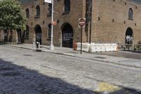 an intersection with a brick road and building in background and another street sign near by